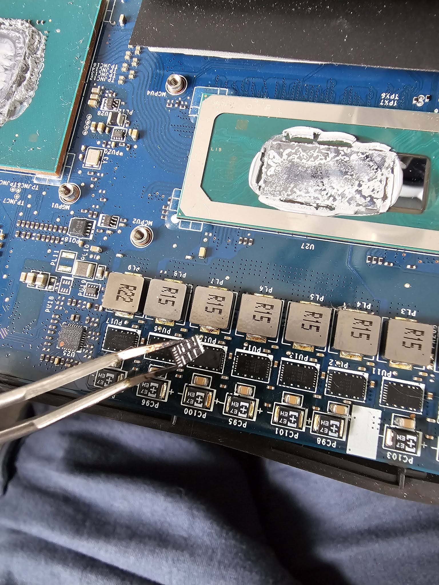 Petit composant DrMOS tenu à la pince devant l’étage d’alimentation du processeur MSI